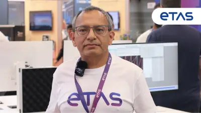 エキシビジョンブースで、ETASのTシャツとイベントバッジを身につけた人物が、コンピュータのディスプレイの前に立っている。