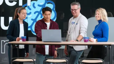 Une équipe diversifiée de quatre professionnels collaborant à un bureau debout et utilisant un ordinateur portable.