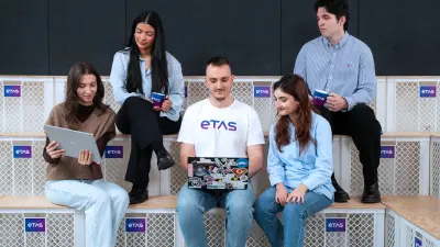 Group of five diverse students sitting casually on modern wooden steps, engaging with a laptop and notebooks in a collaborative environment.