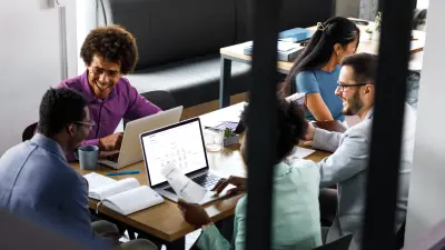 Team works together at a meeting table with laptops.