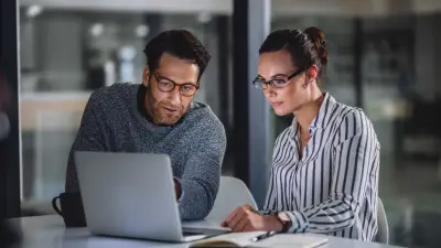 A woman and a man look at a laptop together