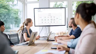 Team discussing at a meeting table and a flat screen with a presentation in front.