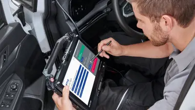 Technician using ETAS diagnostic software on a Getac tablet inside a vehicle.