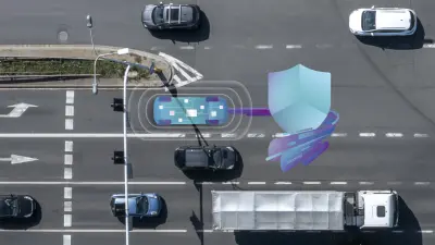 Two colleagues collaborate in a brightly lit, modern office. A woman leans over to offer assistance to a man seated at a desk, who is using a computer mouse. Multiple computer monitors are visible, suggesting a technology-focused workspace.