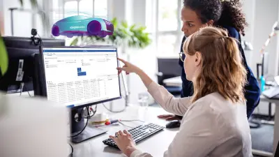 近代的なオフィスのコンピューターで、仮想化ソフトウェアと自動テストソフトウェアの共同開発を行う2人の女性ソフトウェア・エンジニア。