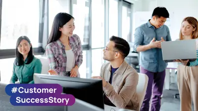 Des membres d'une équipe travaillant ensemble autour de postes de travail informatiques dans un bureau arborant le hashtag #CustomerSuccessStory.