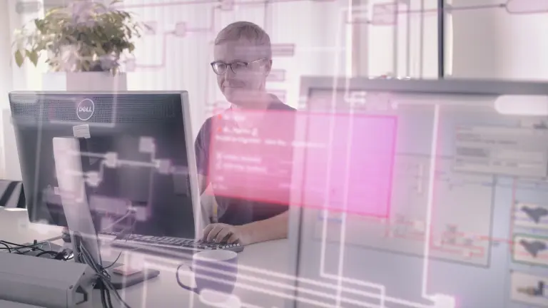 The video shows a developer becoming frustrated with coding errors she does not understand. A coworker is handing her manuals. EHANDBOOK helps her understand the code and makes her work easier.